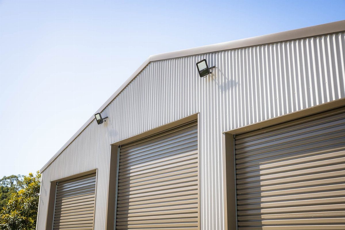 10 Shed Colors Ideas to Paint Your Backyard Storage 5 Tan corrugated metal building with three large roll-up garage doors under a clear sky.