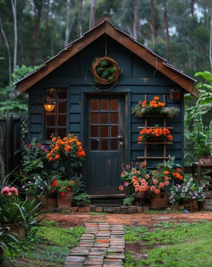 10 Shed Colors Ideas to Paint Your Backyard Storage 2 A dark forest green wooden garden shed surrounded by blooming orange flowers and greenery.