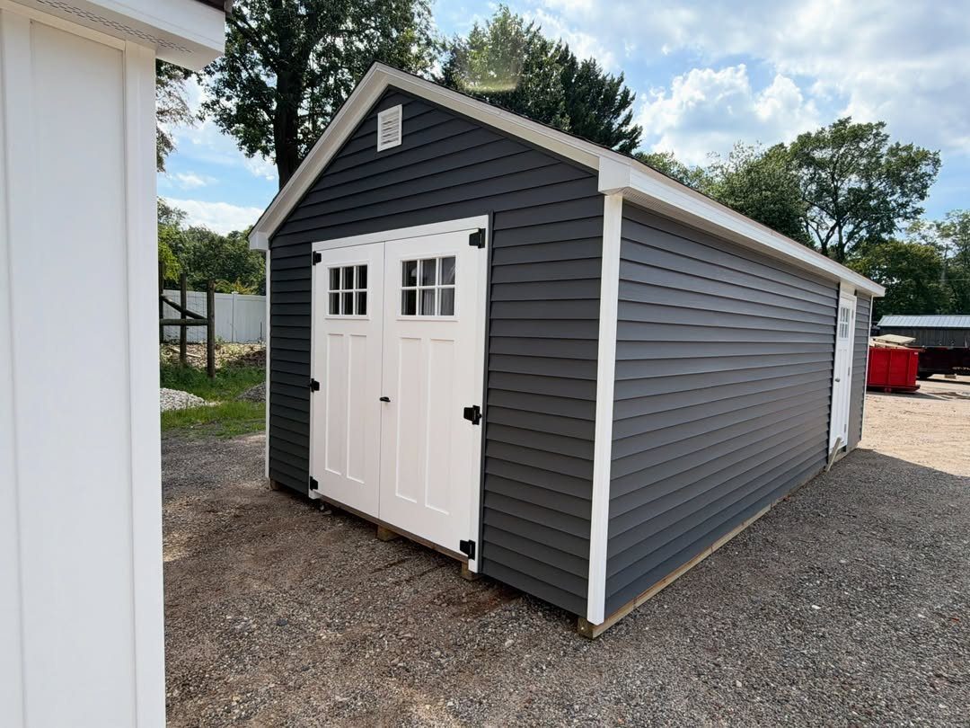 10 Shed Colors Ideas to Paint Your Backyard Storage 8 A charcoal gray garden shed with white trim and white double doors on gravel.