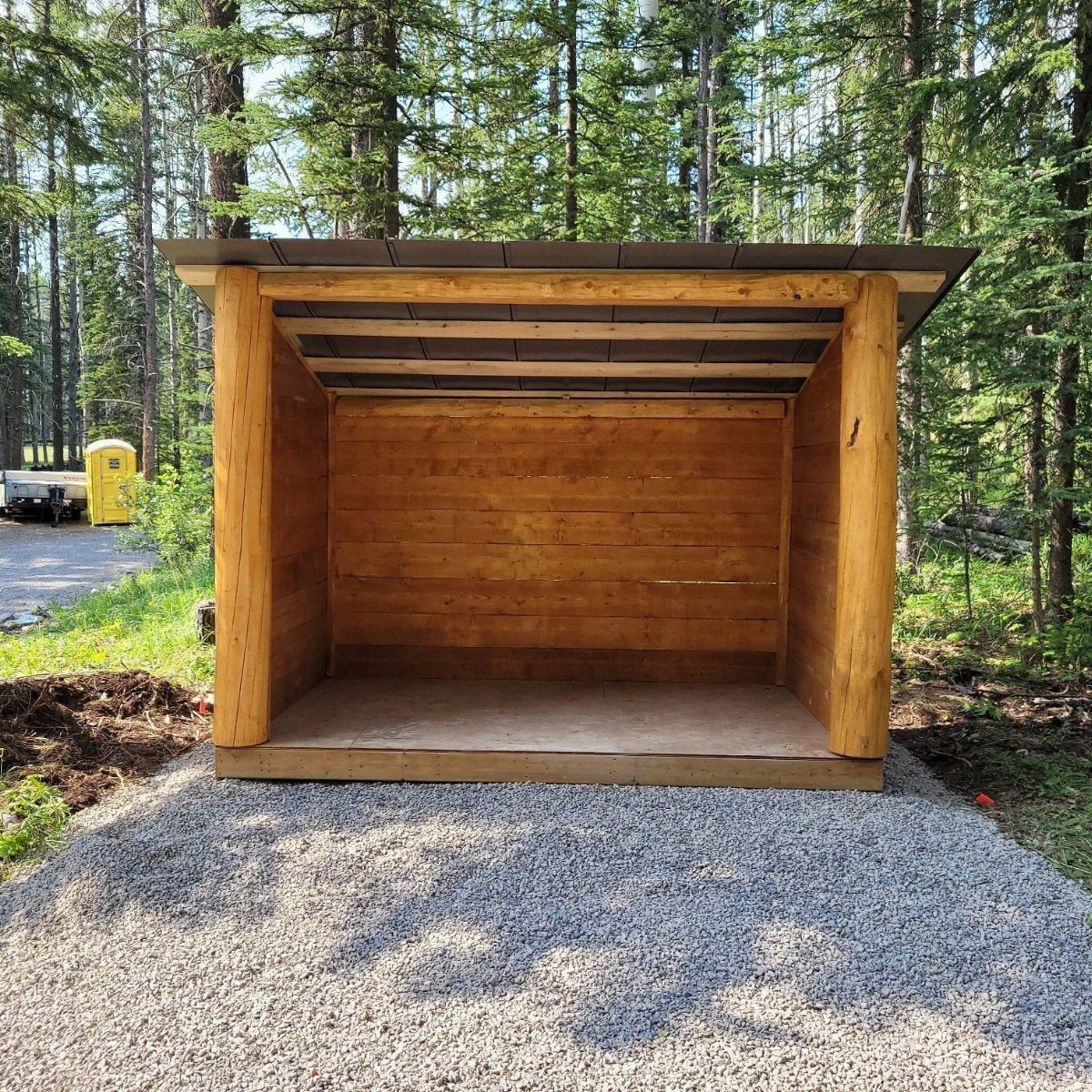 10 Shed Colors Ideas to Paint Your Backyard Storage 6 A rustic wooden log structure with an open front situated in a lush green forest.