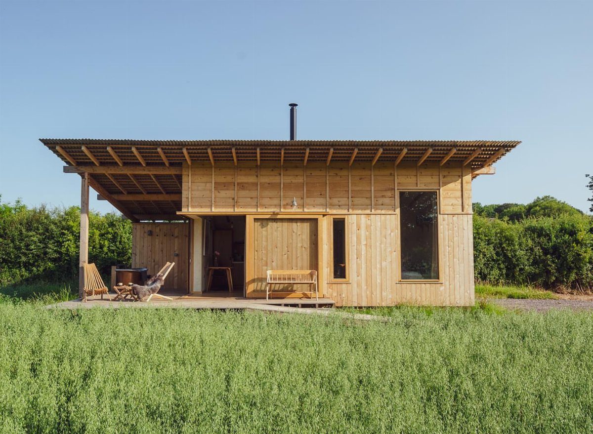 9 Shed Exterior Ideas: Metal, Wood, Recycled, and Garden Styles 9 A modern wooden garden shed with a covered porch and lounge chairs in a green field.