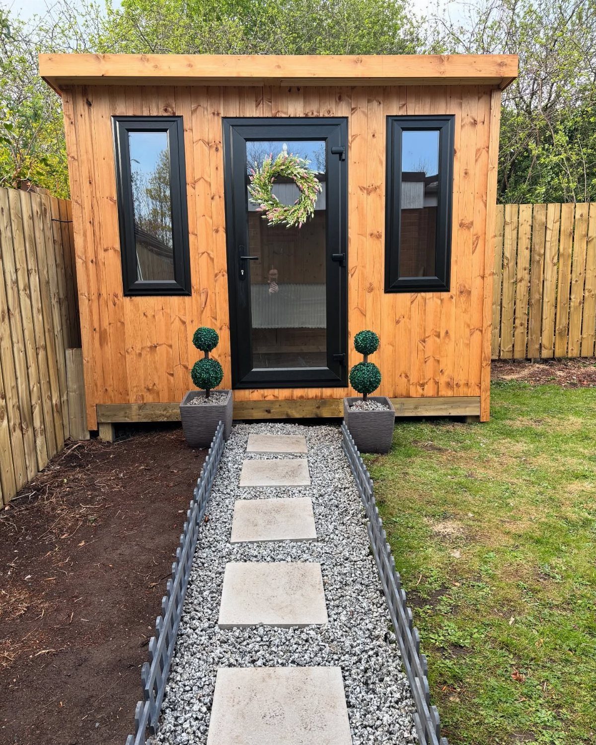 9 Shed Exterior Ideas: Metal, Wood, Recycled, and Garden Styles 8 Wooden garden shed with black windows and a stone pathway leading to the front door.
