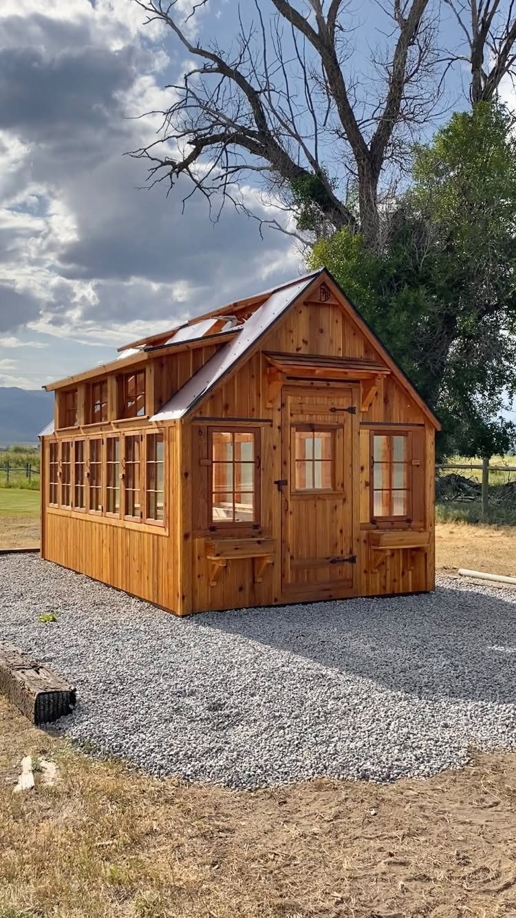 9 Shed Exterior Ideas: Metal, Wood, Recycled, and Garden Styles 7 A small wooden garden shed with many windows sits on a gravel base outdoors.
