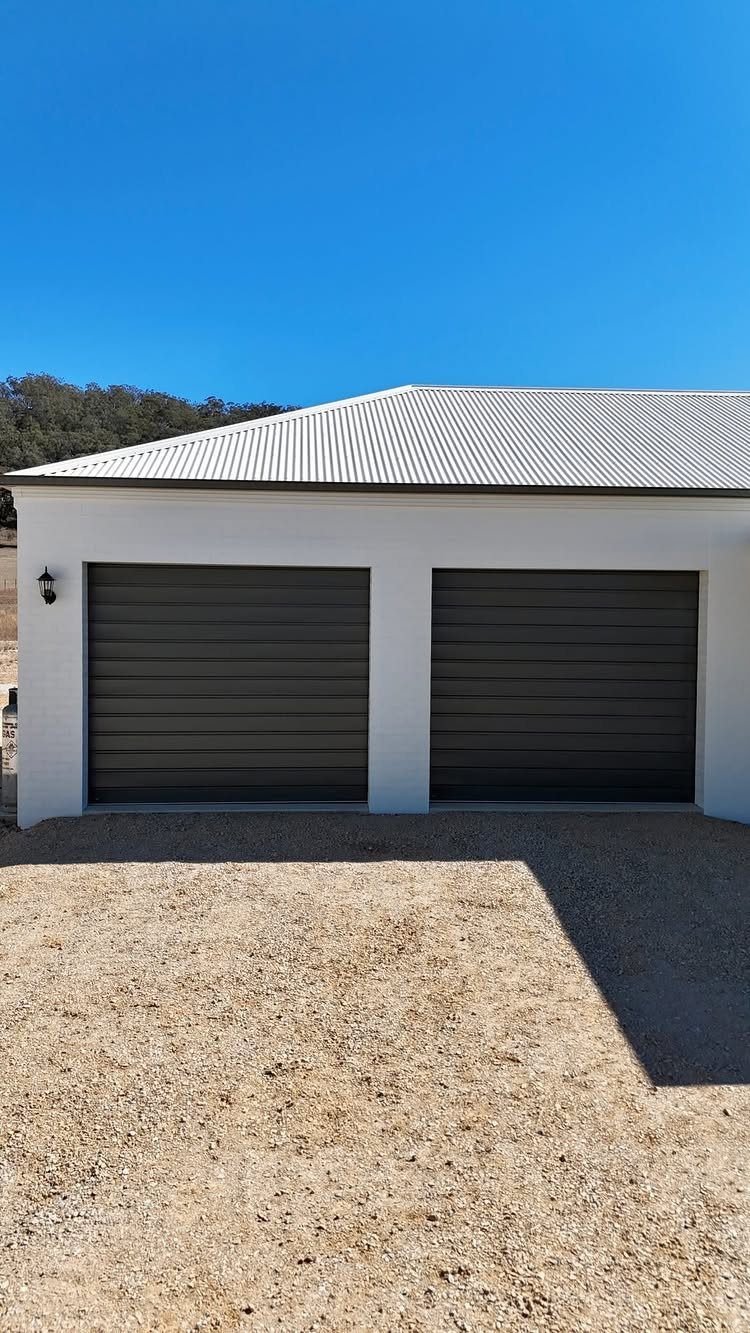 Two dark grey garage doors installed on a white building under a clear blue sky.