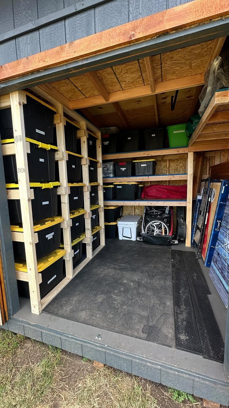 A wooden shed interior organized with black storage bins on vertical racks and shelves.