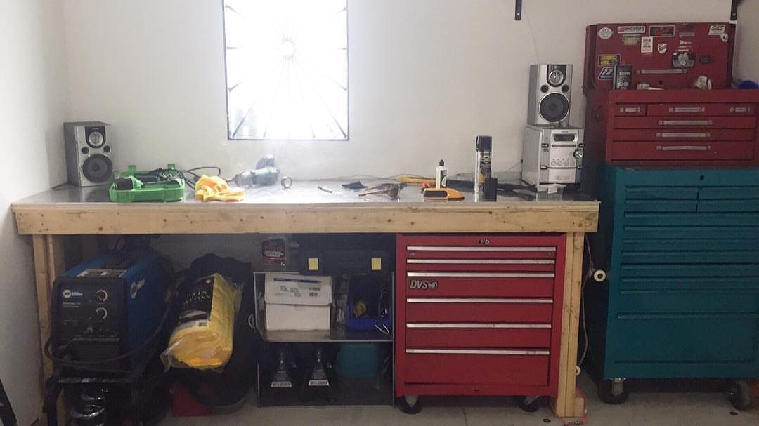 A wooden workbench with various tools on top and storage containers and tool chests underneath.