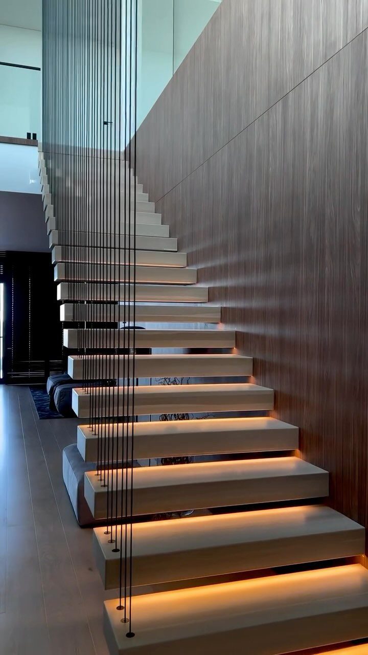 Modern floating wooden stairs with integrated warm LED lighting and thin black cable railings.