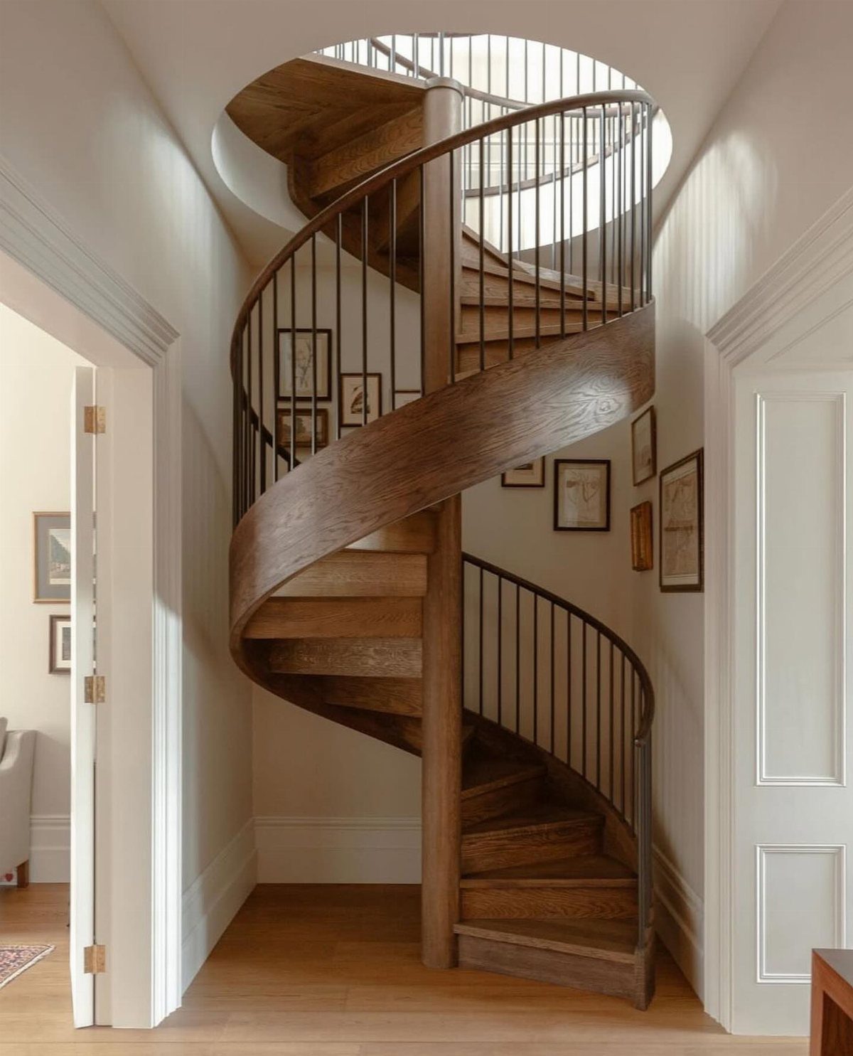 A wooden spiral staircase with dark metal railings stands in a bright white hallway.