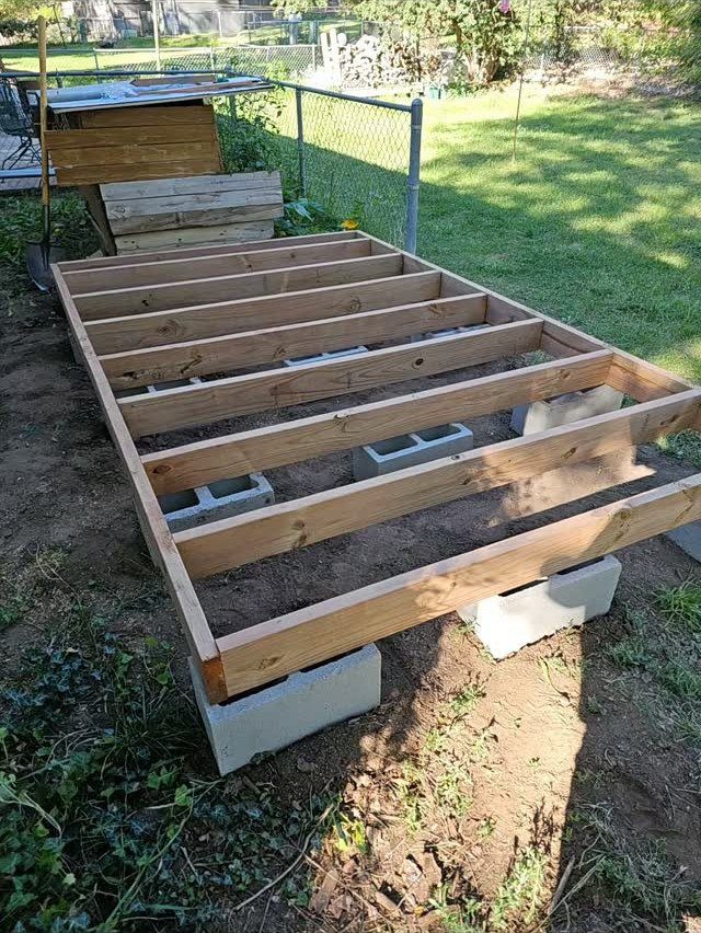 Wooden floor joists resting on grey concrete cinder blocks in a backyard setting.