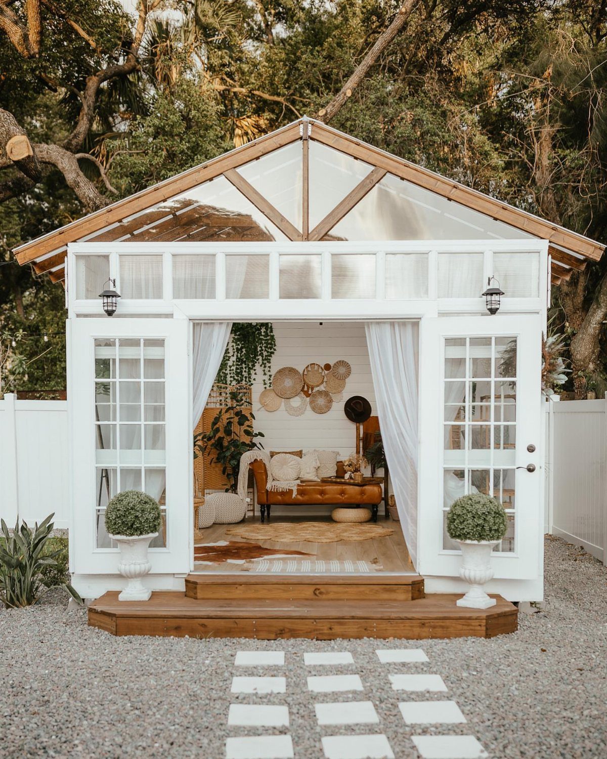 White wooden garden shed featuring large glass windows and a transparent gable overlooking a cozy interior.