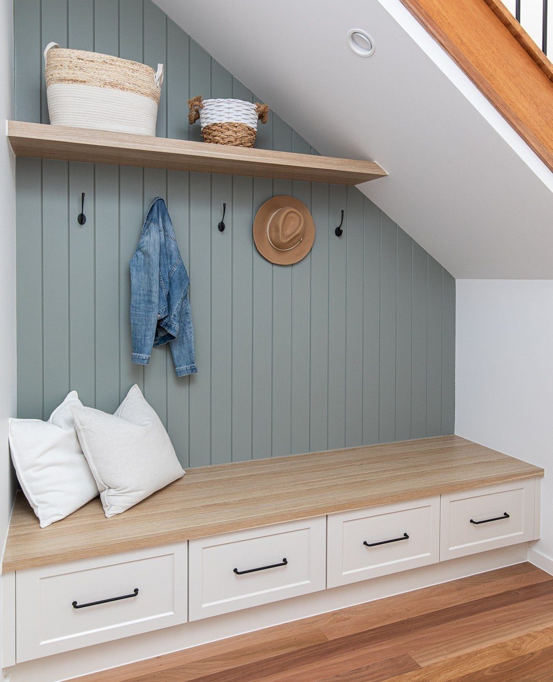 18 Under Stair Storage Design Modern Ideas for Every Home 7 Built-in mudroom bench with white drawers, wooden top, and grey paneled wall with hooks and shelving.