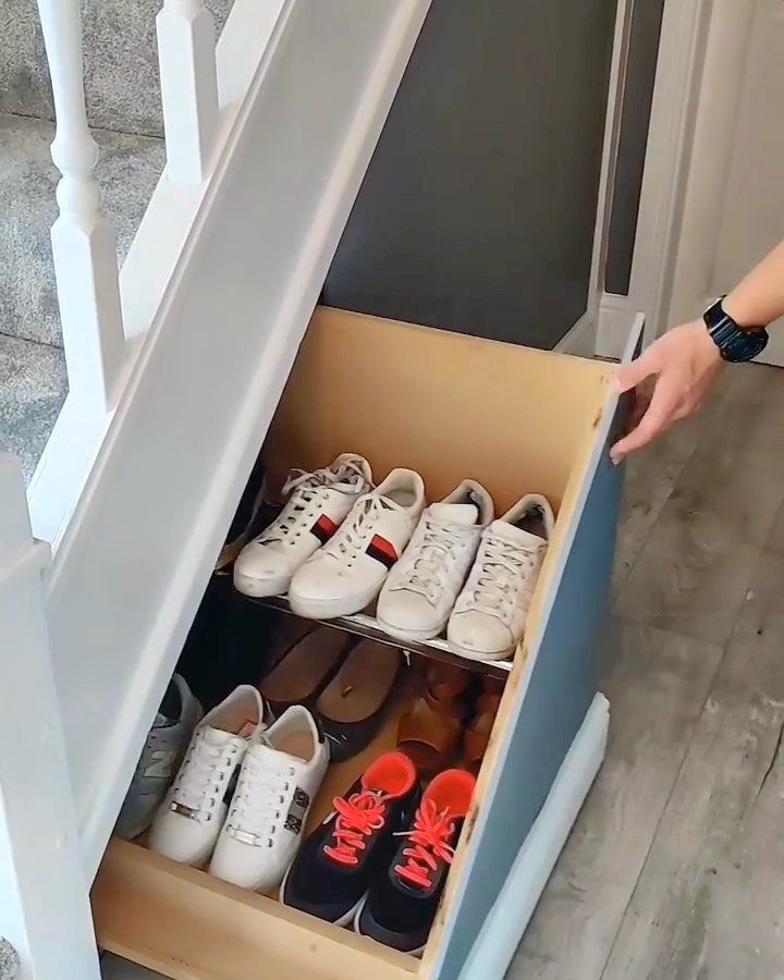 18 Under Stair Storage Design Modern Ideas for Every Home 9 A pull-out wooden drawer under white stairs filled with various pairs of sneakers and shoes.