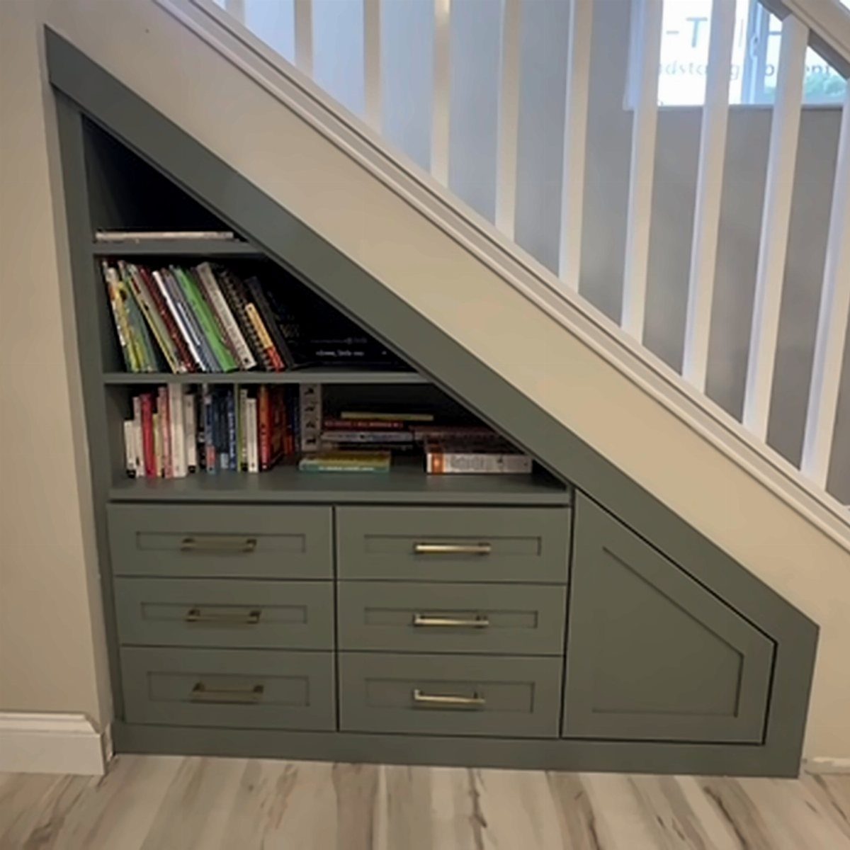Grey built-in shelves and drawers installed underneath a white staircase filled with books.