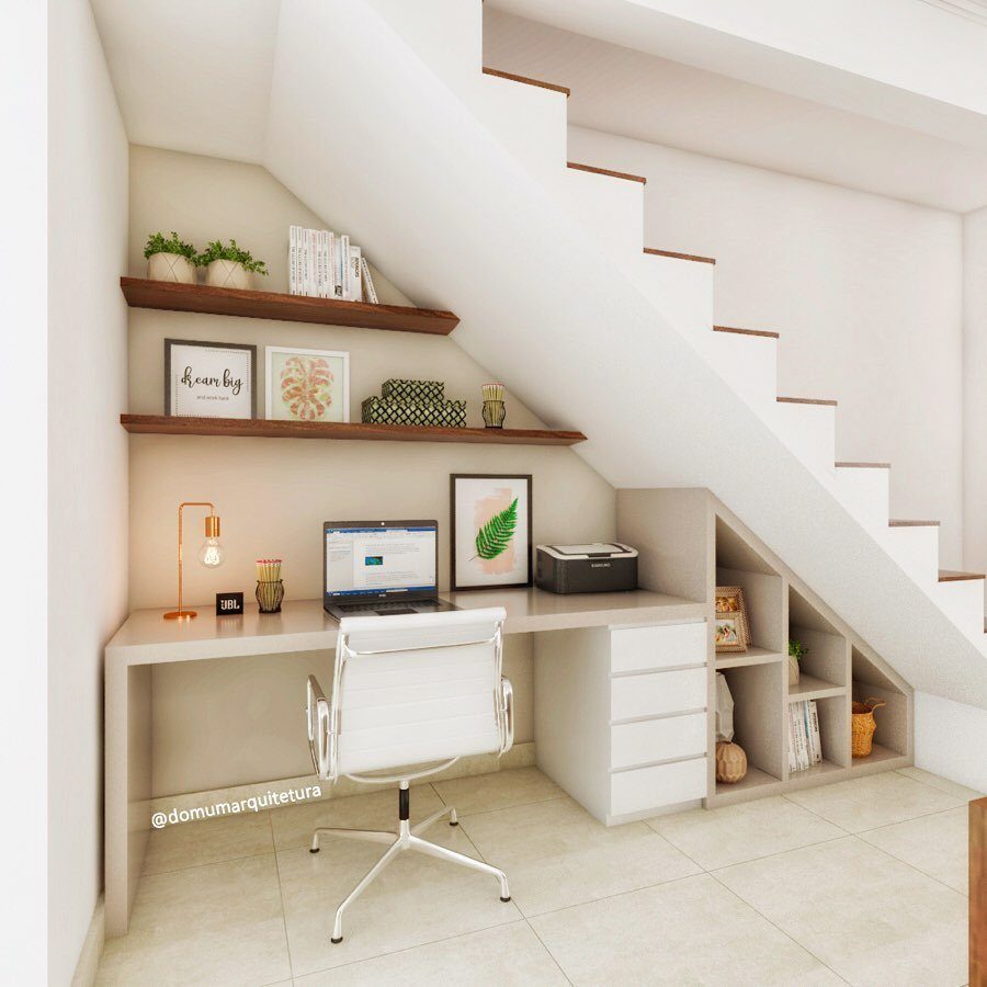 A white built-in desk with drawers and a chair located under a white staircase.