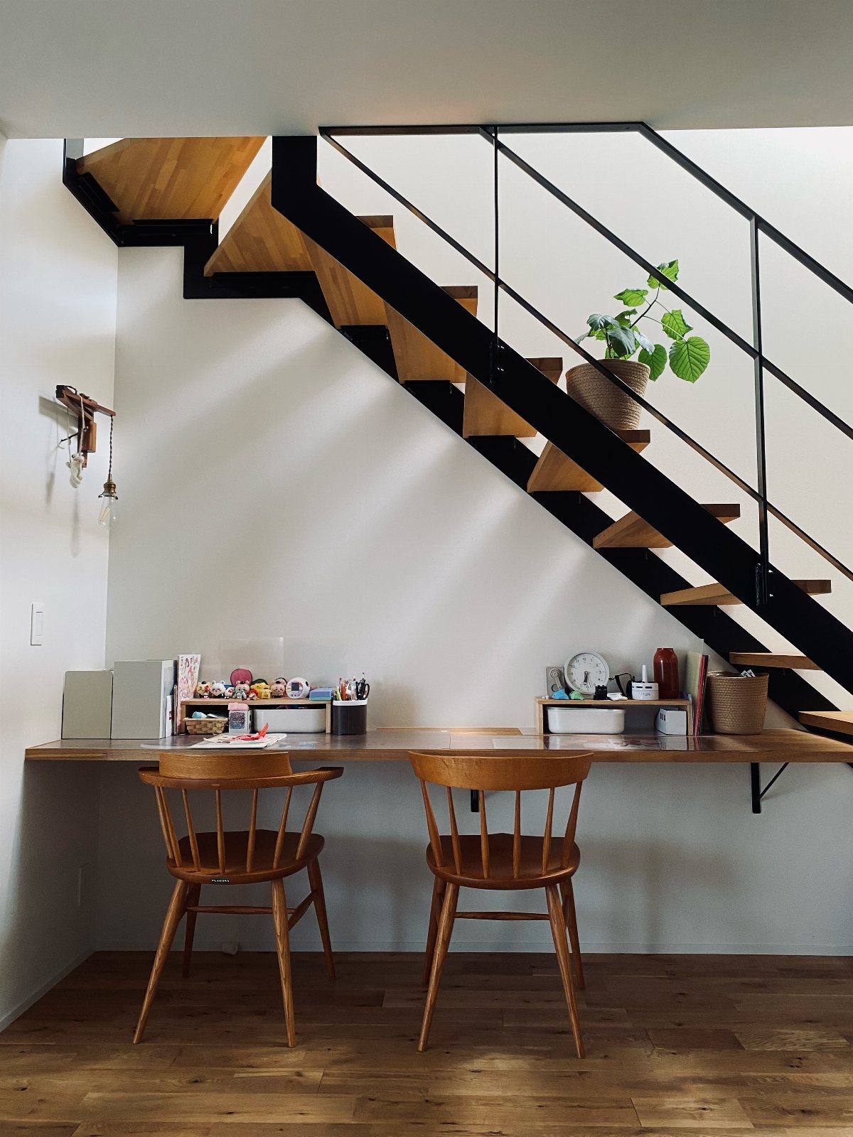 A long wooden floating desk with two chairs positioned under a modern staircase.