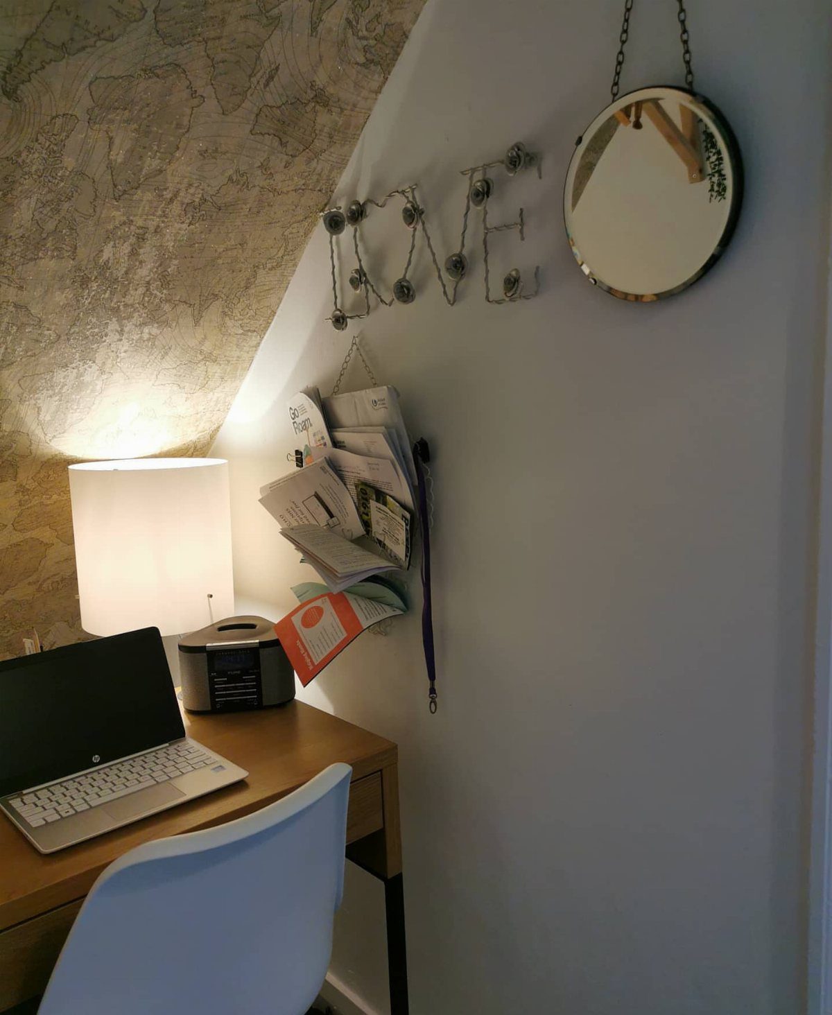 A small desk workspace under a sloped ceiling featuring a LOVE sign and a round mirror.