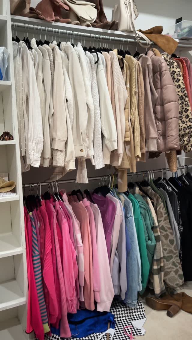 Clothing hanging on two tiers of an open wardrobe, organized by color from white to pink and teal.