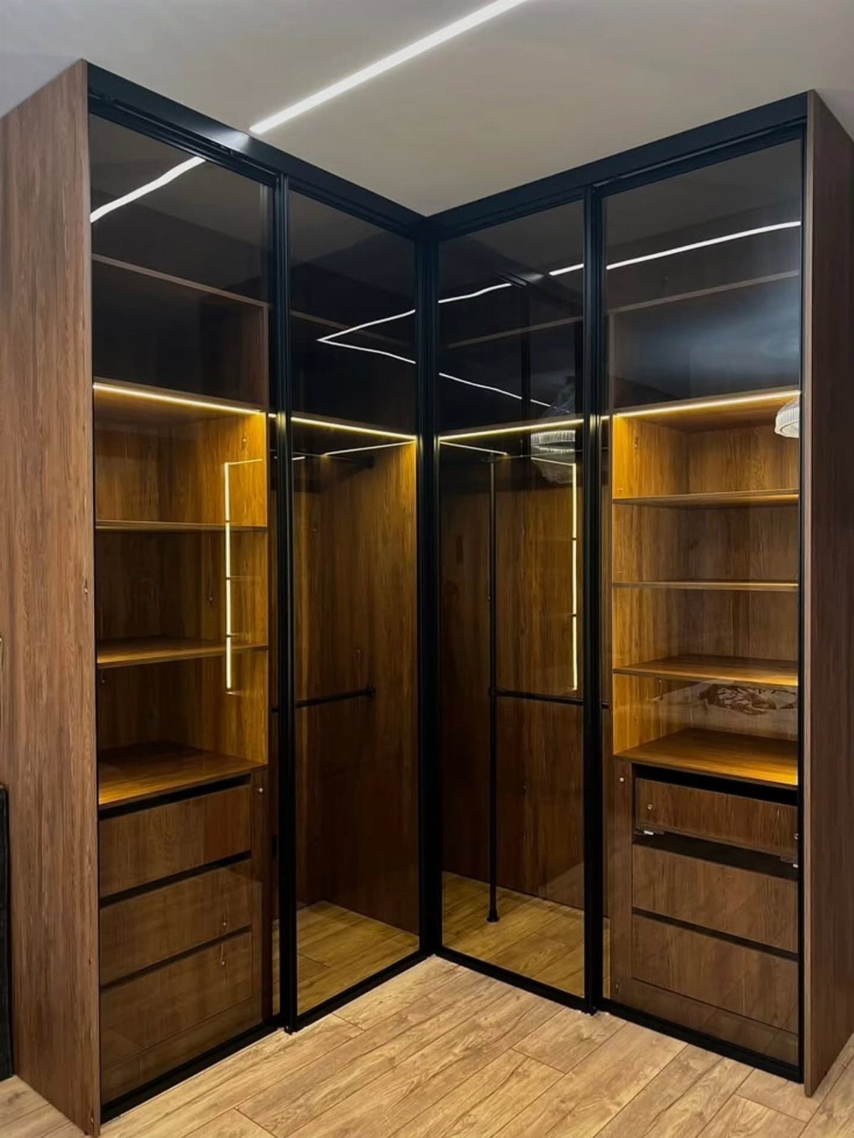 Corner wardrobe with dark wood frames, glass doors, and warm interior lighting.