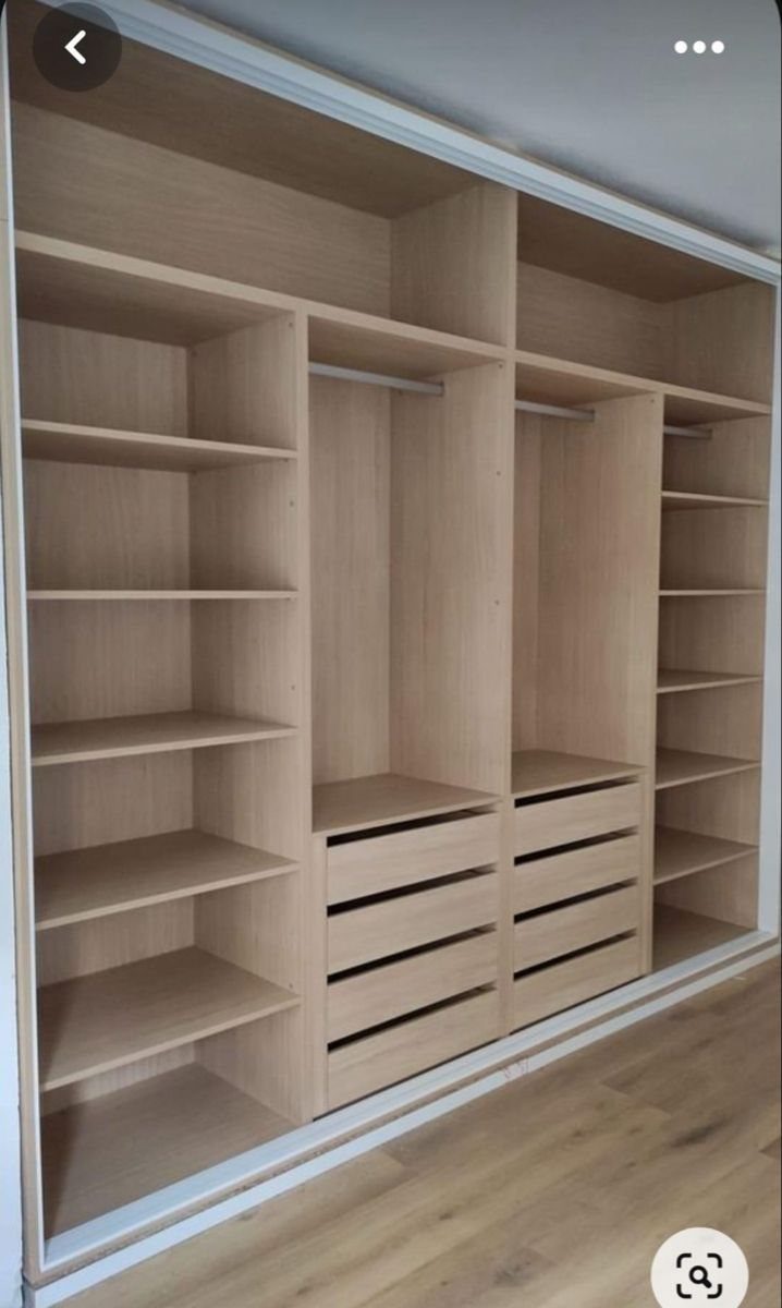 Light wood laminate wardrobe with open shelving, hanging rods, and built-in drawers against a white wall.