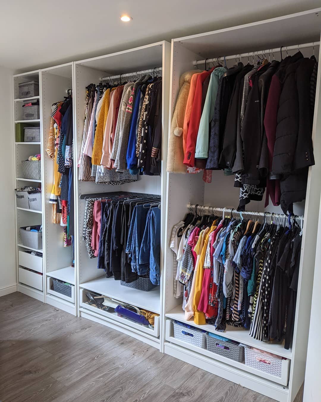 White built-in open wardrobe system with hanging clothes and storage bins on shelves.