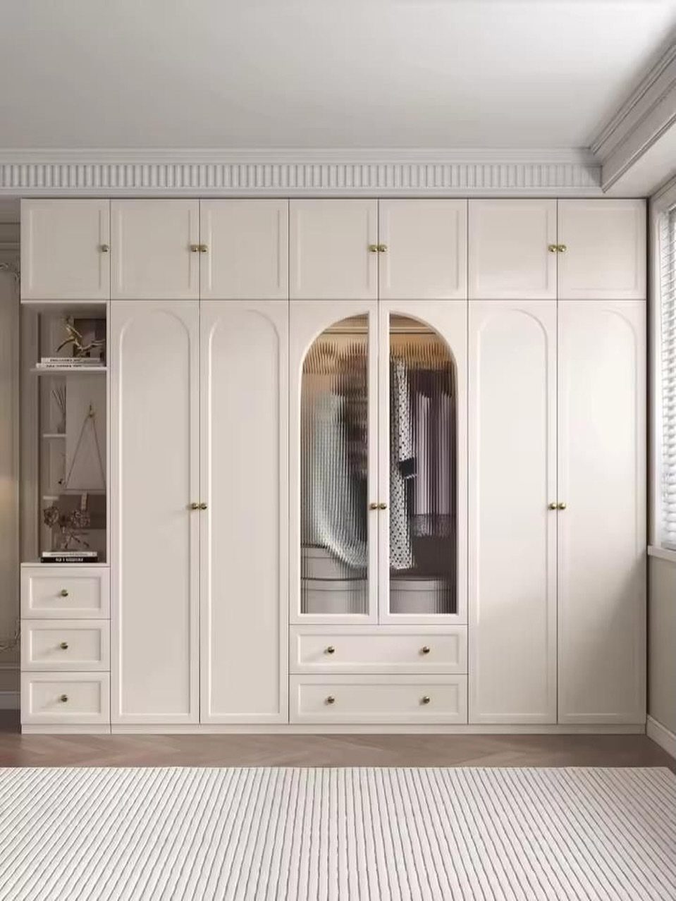 White built-in wardrobe with arched doors, gold handles, and glass panels showing clothes inside.