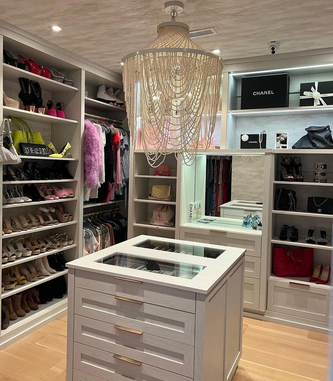 White built-in closet shelving filled with luxury accessories and a central white storage island.
