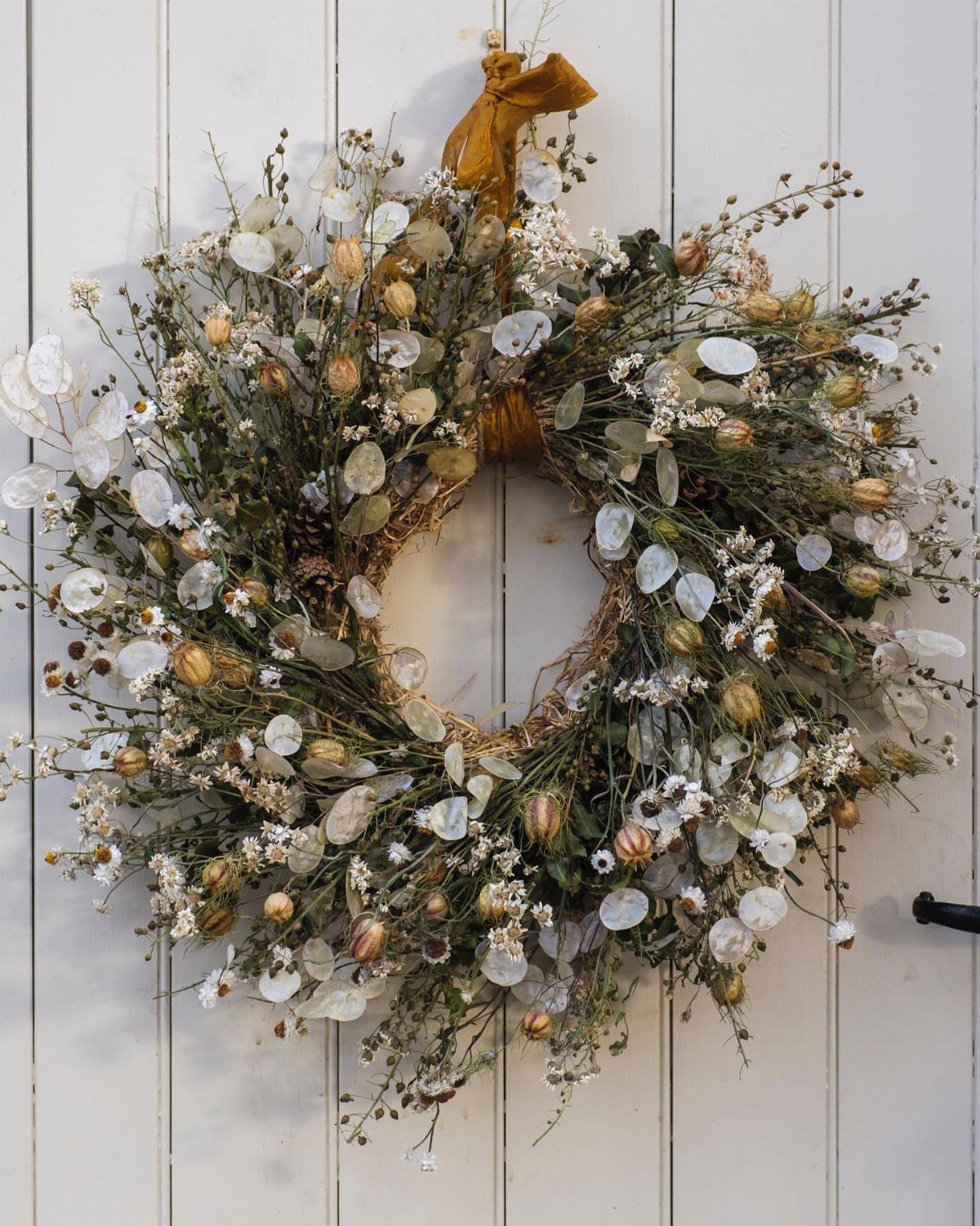 A decorative wreath composed of dried flowers and white blossoms hanging on a white wooden door.