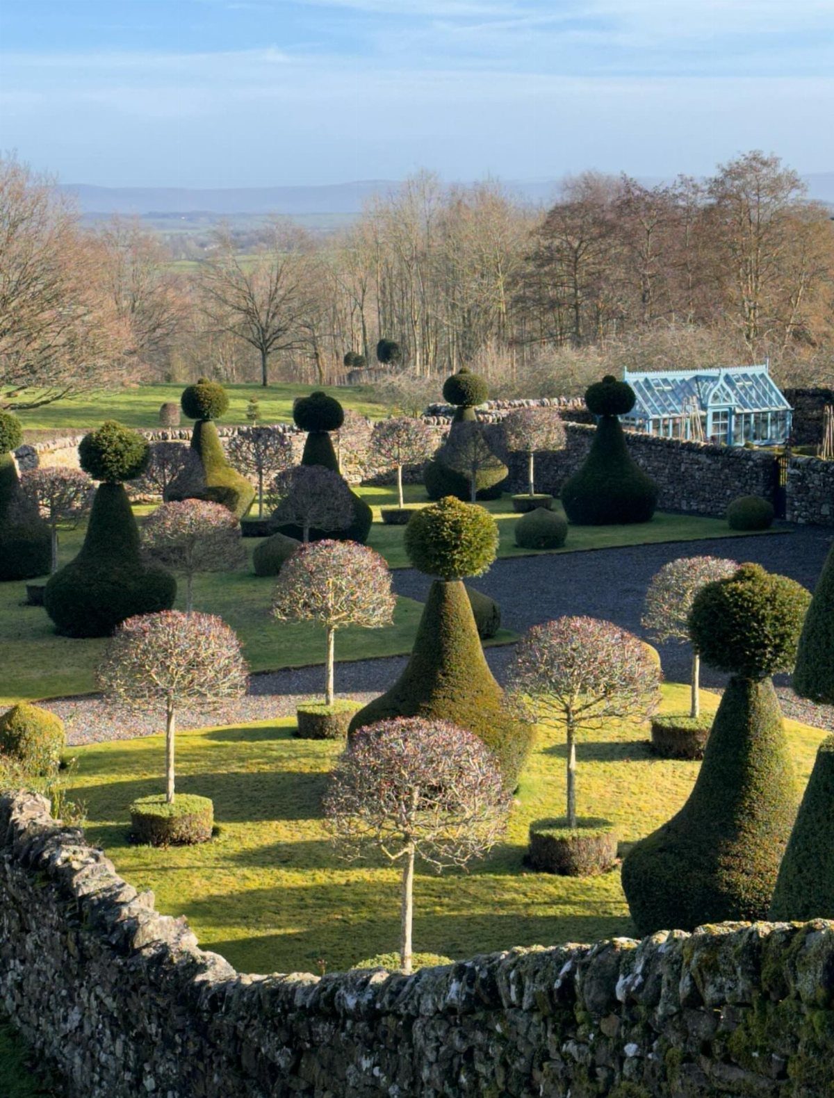 Manicured topiary shrubs in various geometric shapes scattered across a green garden lawn.