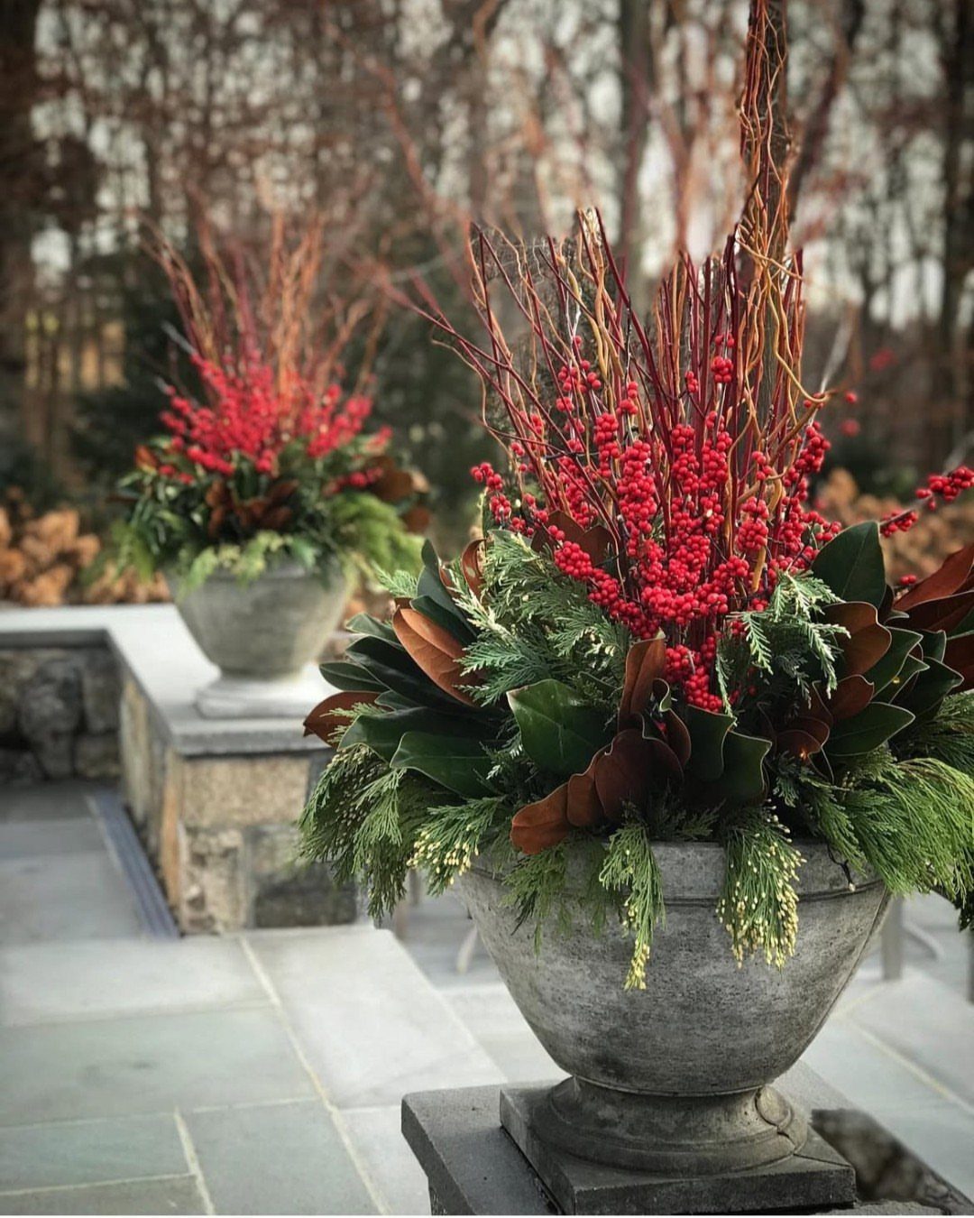 Stone urns filled with red berries, evergreen branches, and magnolia leaves on a stone patio.