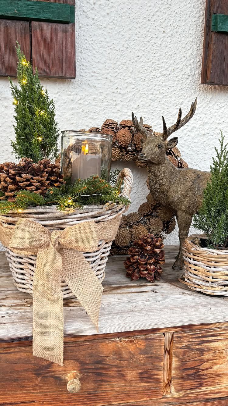 A white wicker basket containing evergreen branches, pinecones, and a lit candle in a glass holder.