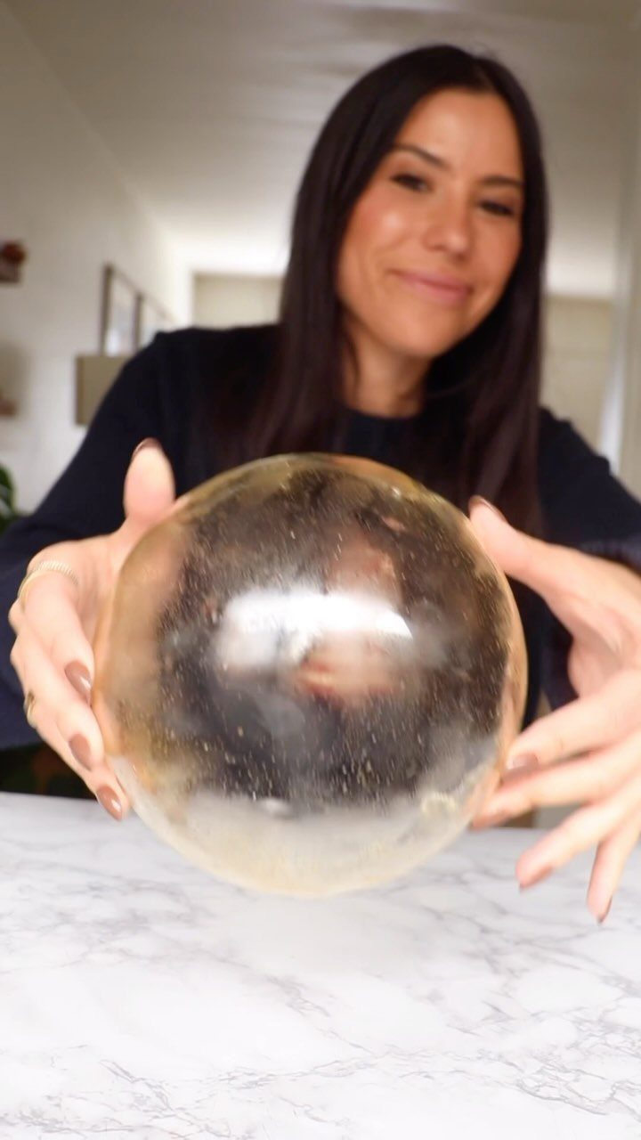 A woman holding a clear plastic bakery cake dome over a marble tabletop.